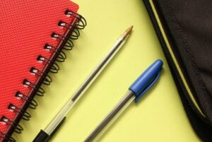 black and blue pens beside red covered notebook